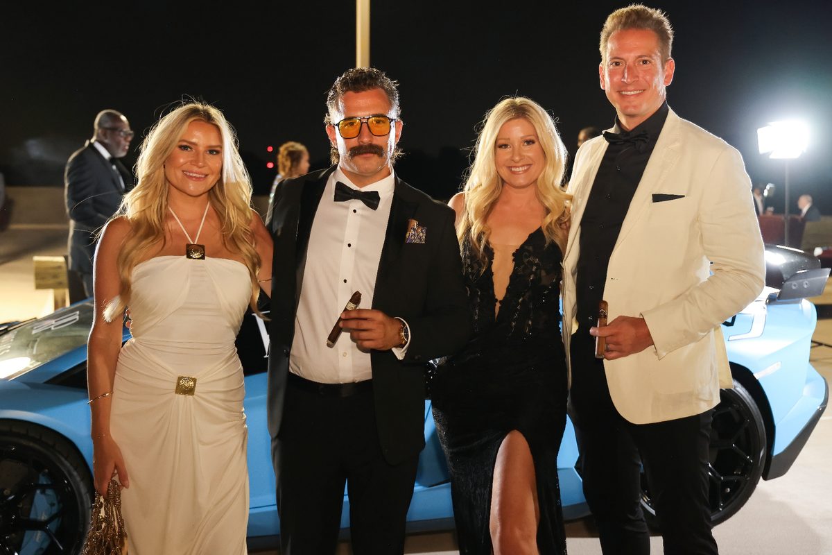 Four guests posing with a blue supercar at the black-tie gala