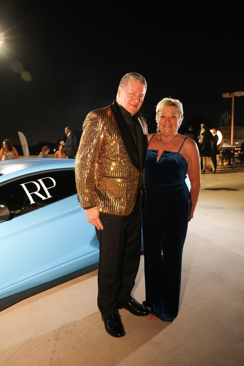 Guest in a gold tuxedo jacket beside a blue supercar