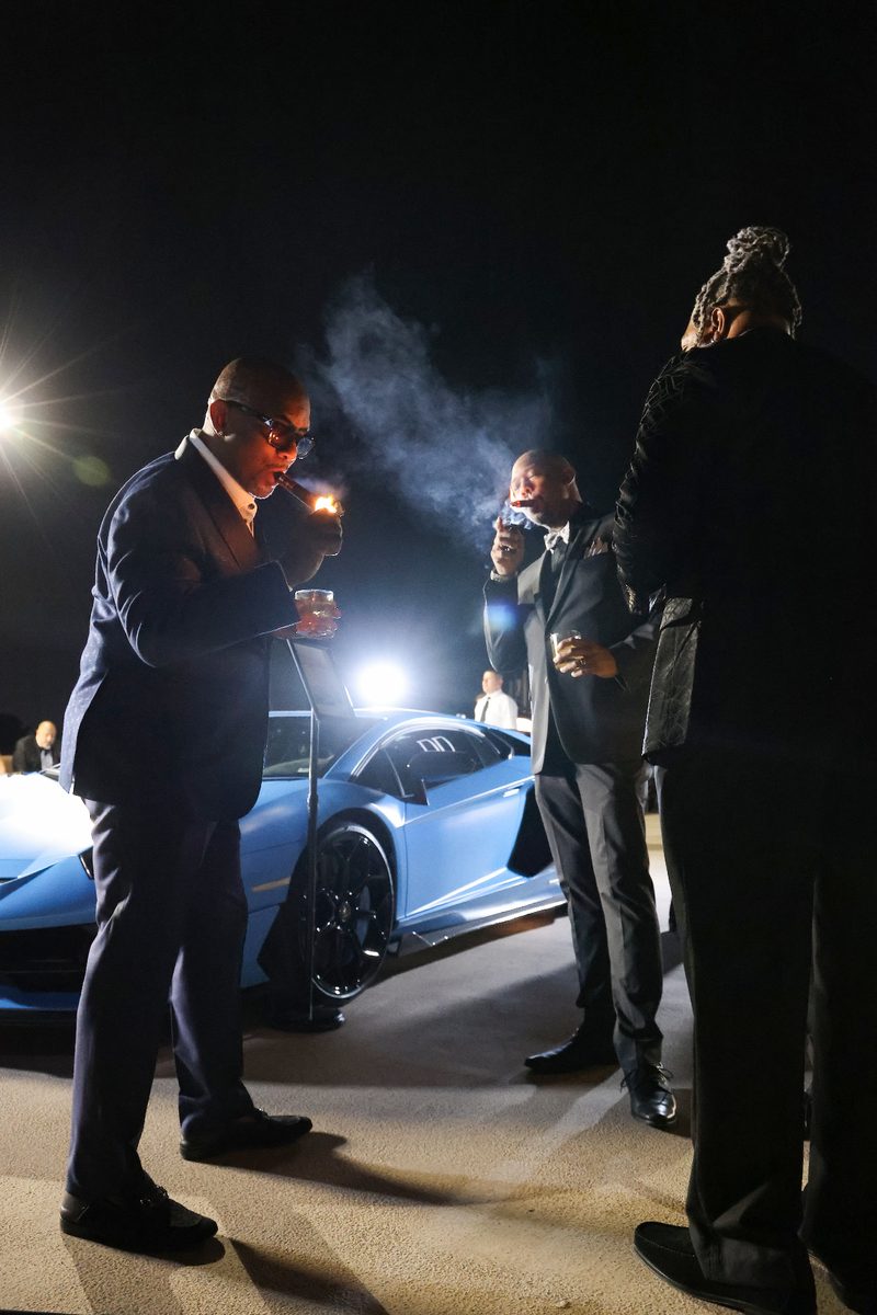 Guest beside a blue supercar amid stage haze
