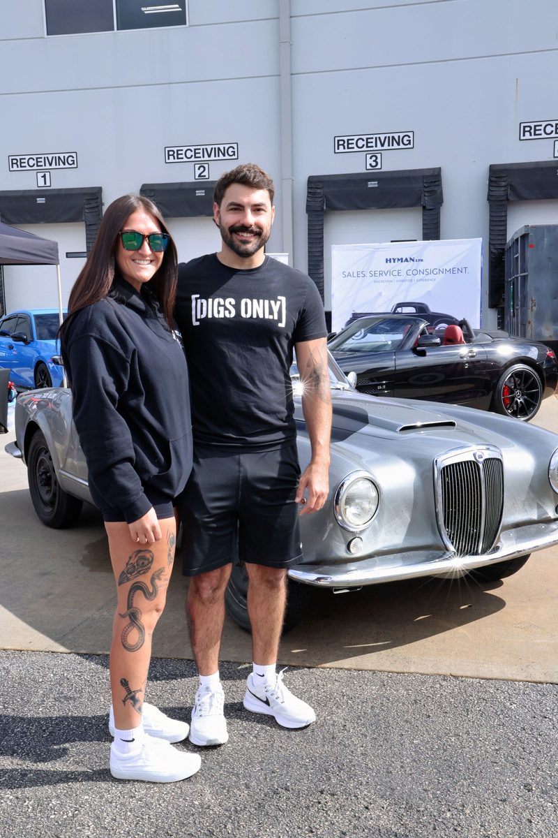 Couple beside a vintage silver sports car at the car show
