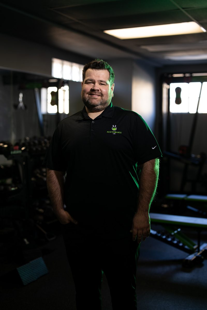 Environmental headshot of a bearded male trainer in a fitness gym