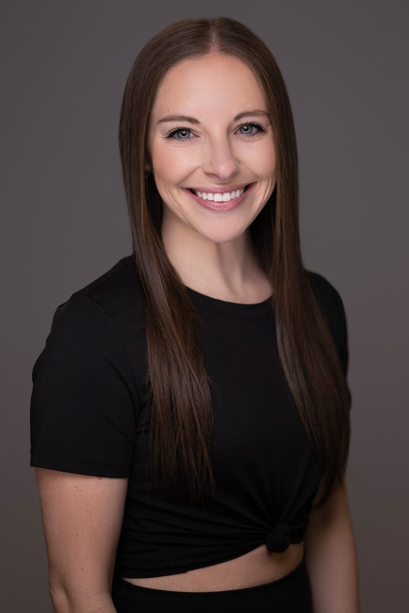 Studio headshot of a woman in a grey blazer on a dark background