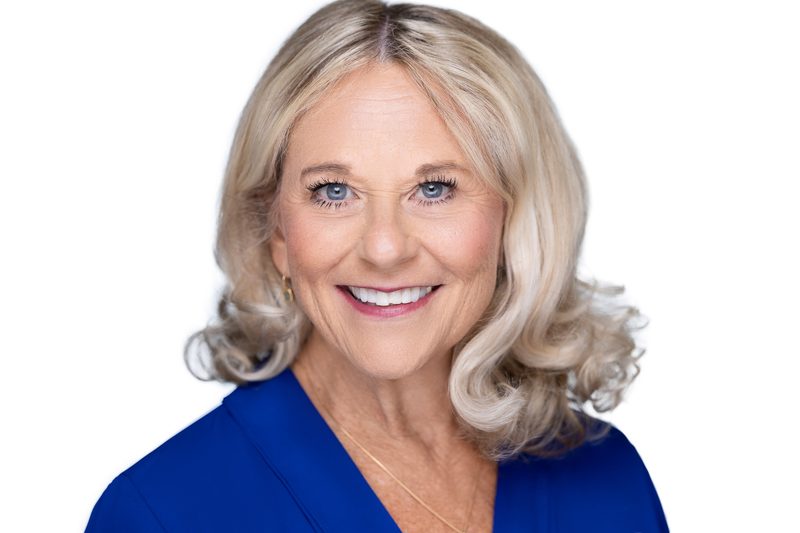 Studio headshot of a smiling woman in a blue top on a white background